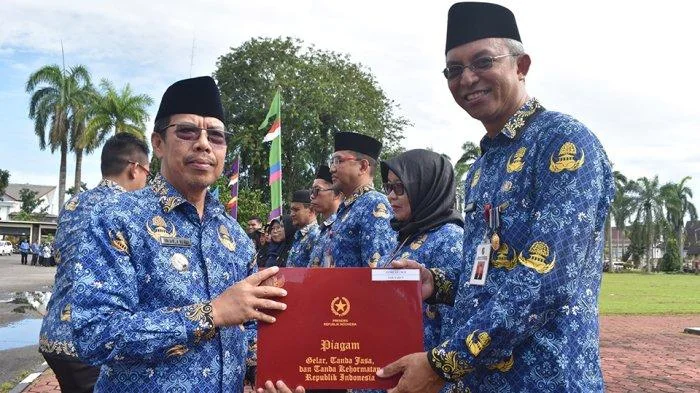 Pj Bupati Mempawah Ismail menyerahkan piagam gelar tanda jasa dan tanda kehormatan Republik Indonesia kepada Kepala Badan Pengelola Pajak dan Retribusi Daerah, Yusri, atas pengabdian selama 30 tahun sebagai ASN, Jumat 29 November 2024.(Tribun)